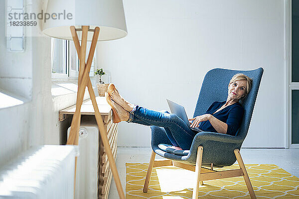 Geschäftsfrau mit Laptop sitzt auf Sessel im Büro