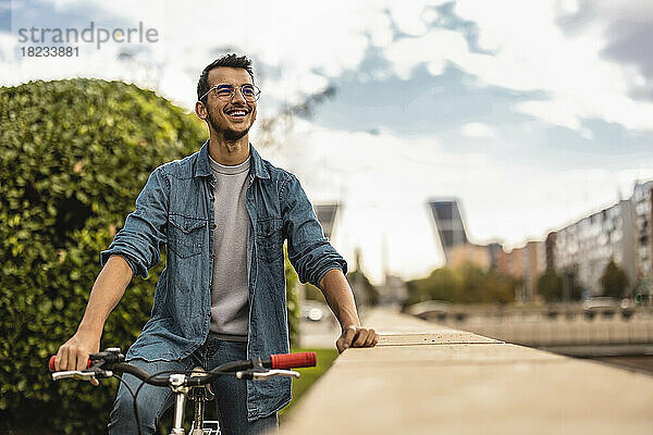 Glücklicher junger Mann sitzt auf dem Fahrrad unter bewölktem Himmel