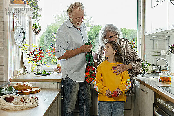 Großeltern und Enkelin packen frische Lebensmittel in der Küche aus