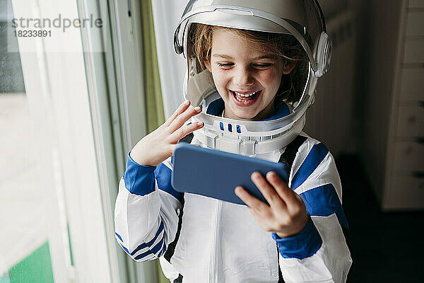 Glückliches Mädchen im Weltraumkostüm  das zu Hause einen Videoanruf auf dem Mobiltelefon führt