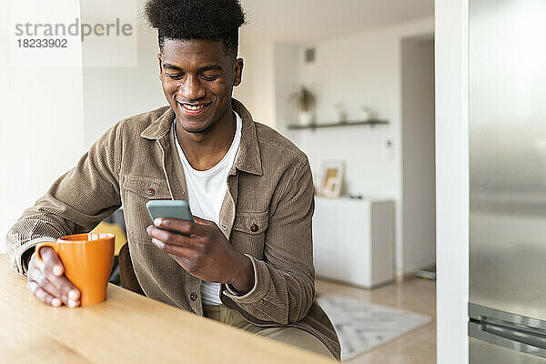 Lächelnder Mann benutzt Smartphone und trinkt zu Hause Kaffee