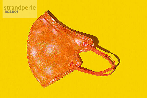 Orangefarbene FFP2-Maske vor gelbem Hintergrund