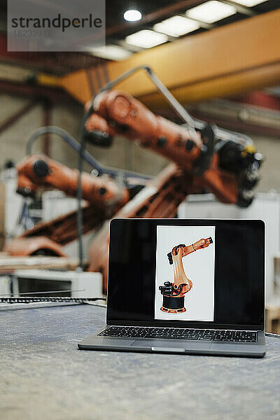 Laptop mit Roboterarmbild am Schreibtisch in der Industrie