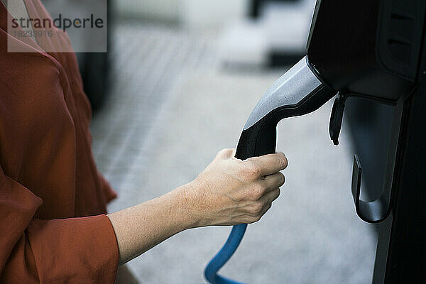 Hand einer Frau  die den Stecker des Ladegeräts für ein Elektroauto hält