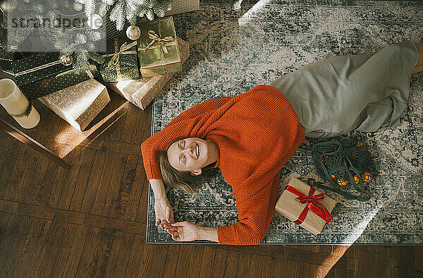 Lächelnde Frau  die sich zu Hause auf den Teppich legt