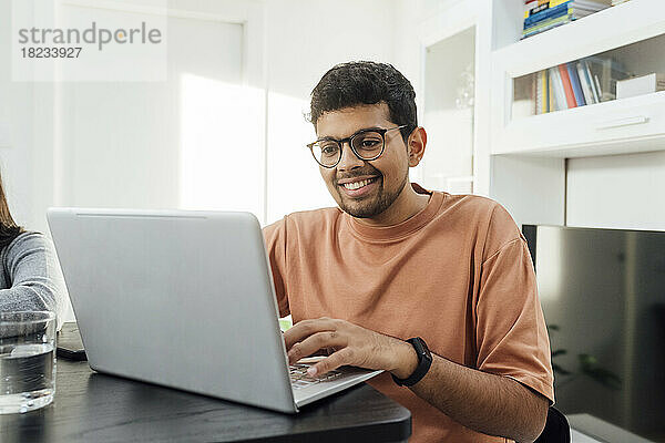 Happy man studying through laptop on table in living room