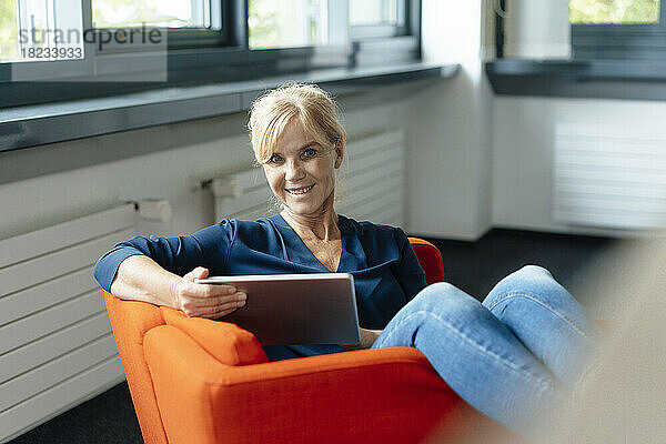 Glückliche Geschäftsfrau mit Tablet-Computer auf Sessel im Büro