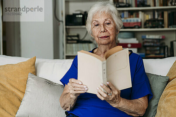 Ältere Frau liest zu Hause auf dem Sofa ein Buch