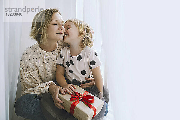 Mutter und Tochter mit Weihnachtsgeschenk sitzen vor dem Vorhang