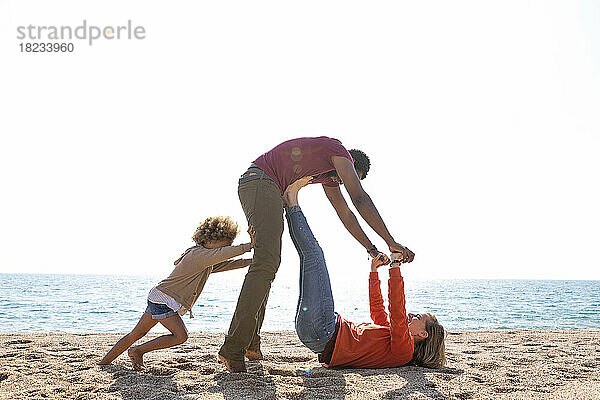Glückliche Frau spielt mit Mann und Tochter am Strand