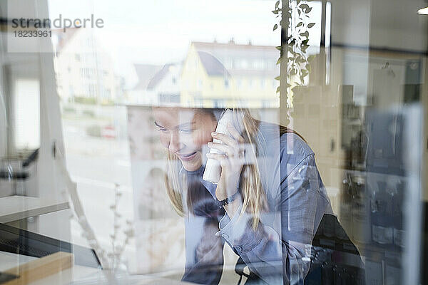 Lächelnde Frau  die am Telefon spricht und durch die Glasscheibe im Friseursalon gesehen wird