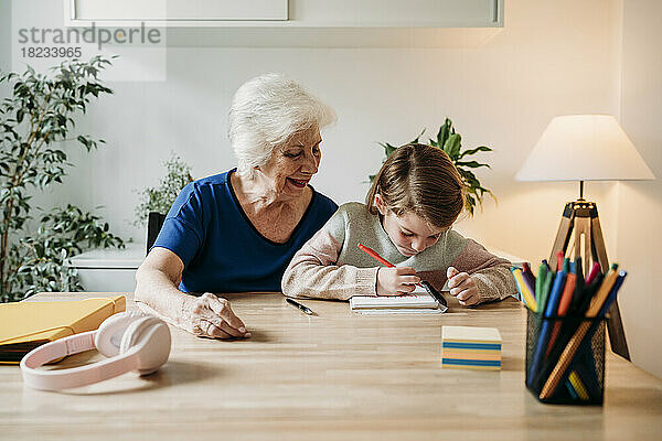 Lächelnde Großmutter hilft Mädchen beim Lernen am Tisch zu Hause
