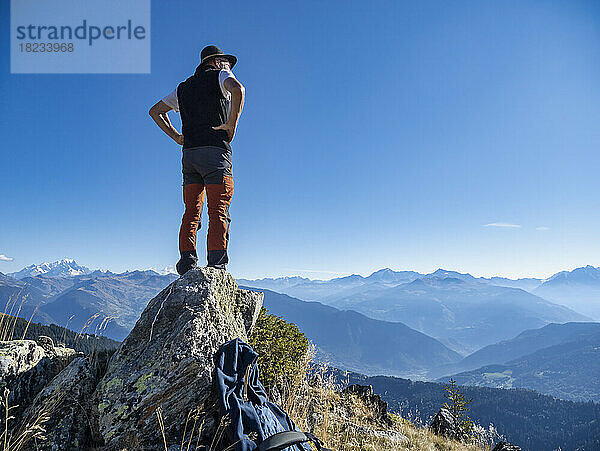 Älterer Mann mit den Händen auf der Hüfte steht auf einem Felsen unter blauem Himmel im Nationalpark Vanoise  Frankreich