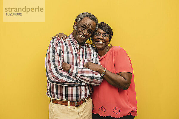 Glückliches älteres Paar  das vor gelbem Hintergrund zusammensteht