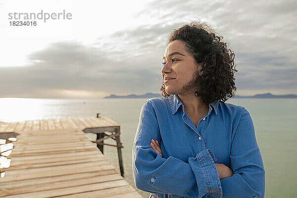 Thoughtful smiling woman standing on jetty at sunset