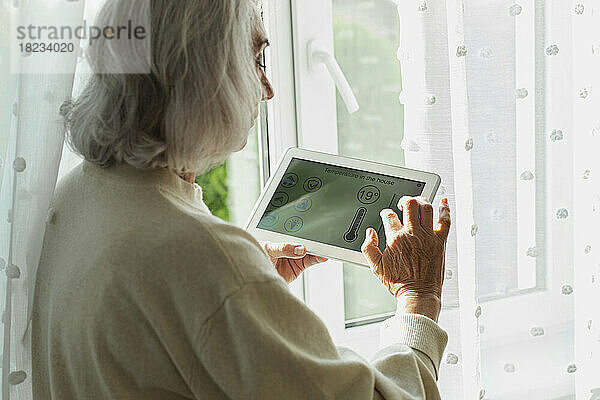 Ältere Frau passt die Temperatur auf einem Smart-Home-Gerät an