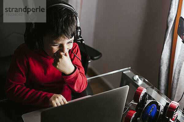 Happy boy wearing headphones using laptop on table