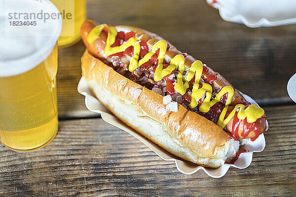Senf und Ketchup auf Hot Dog mit einem Glas Bier am Tisch