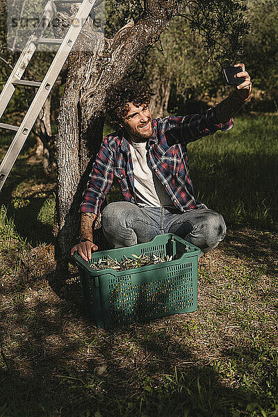 Glücklicher Mann mit Olivenkiste  der ein Selfie mit dem Handy macht