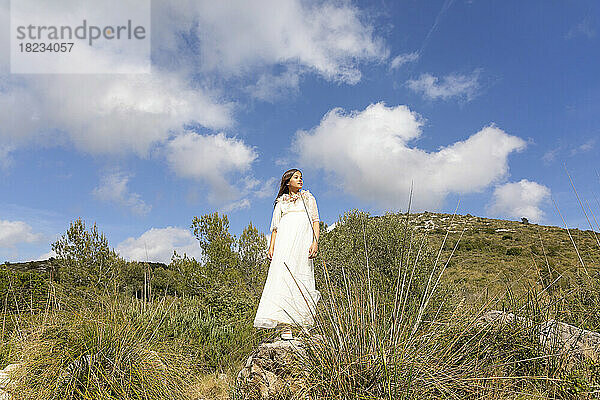 Mädchen im weißen Kleid auf Felsen unter bewölktem Himmel