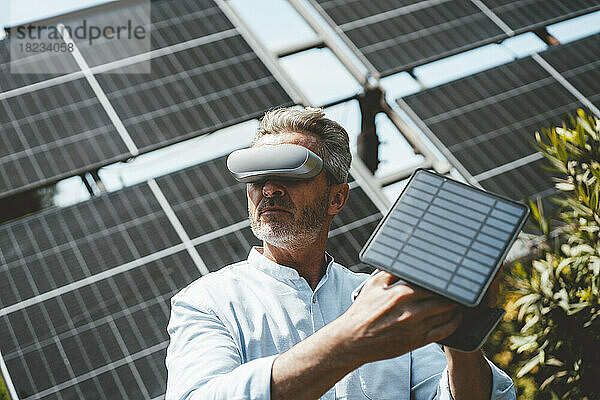 Reifer Mann mit VR-Brille hält Solarpanel im Garten