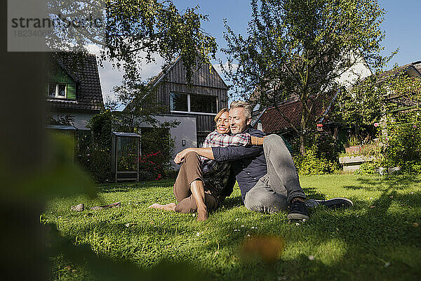 Reife Frau umarmt Mann  der auf Gras im Hinterhof sitzt