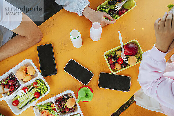 Teenager-Schüler essen zu Mittag und sitzen mit Smartphones am Tisch