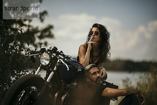Reifer Mann und rauchende Frau lehnen sich an Motorrad