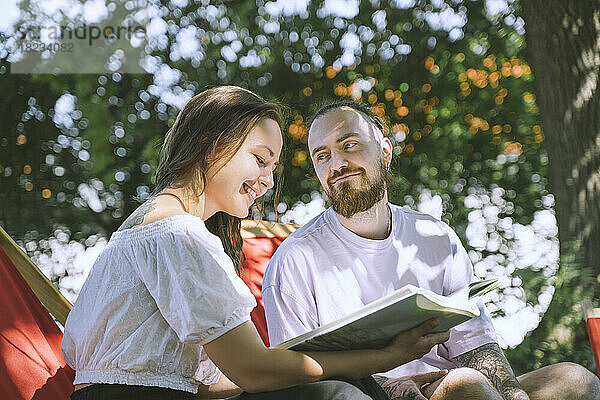 Hipster-Mann blickt lächelnd auf seine Freundin und liest im Hinterhof ein Buch