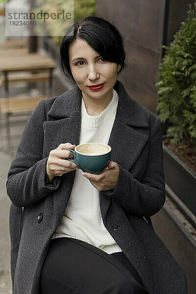 Schöne Frau mit Kaffeetasse sitzt im Straßencafé