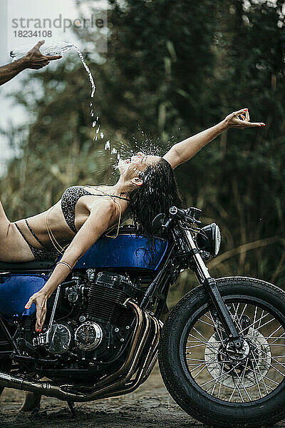 Reifer Mann gießt Wasser in den Mund einer Frau  die auf dem Motorrad liegt