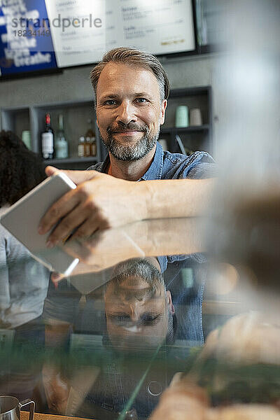 Lächelnder Cafébesitzer mit Tablet-PC steht am Tresen im Café