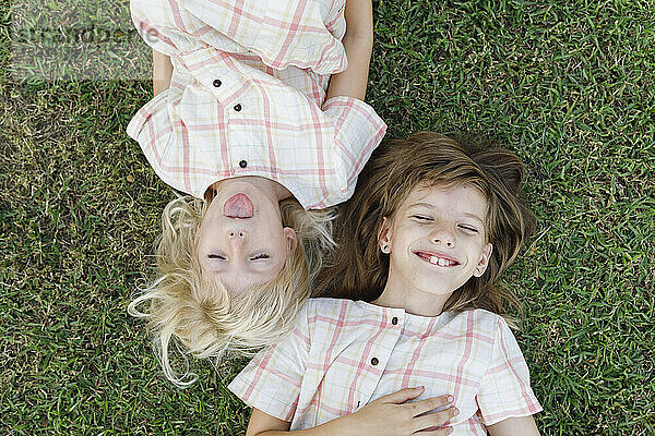 Nettes Mädchen streckt die Zunge heraus und liegt neben ihrer glücklichen Schwester im Gras