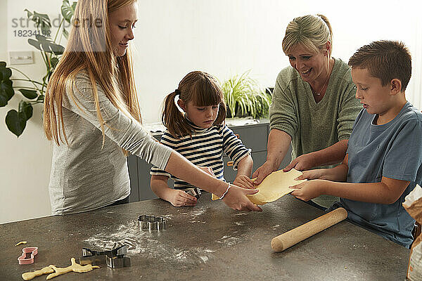 Happy mother with children holding rolled dough at home