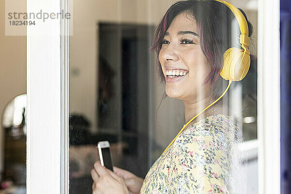 Glückliche junge Frau mit Kopfhörern  gesehen durch Glasfenster