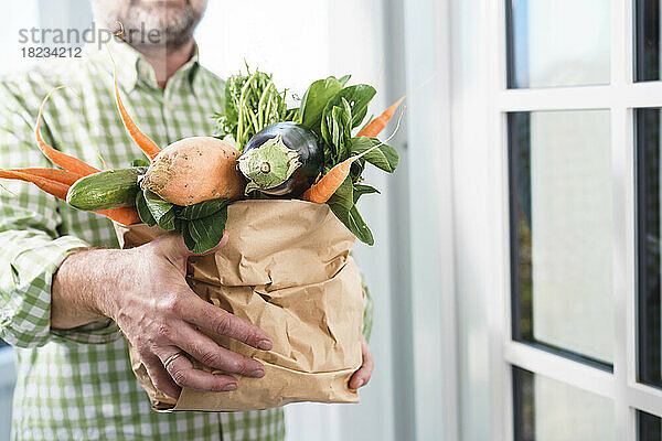 Reifer Mann hält Papiertüte mit frischem Gemüse vor der Tür