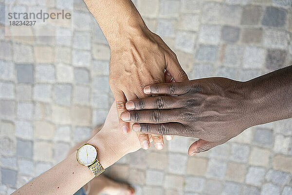 Multiracial friends stacking hands over footpath