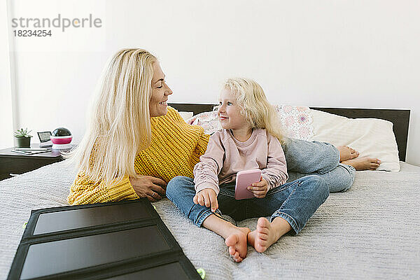 Glückliche Mutter und Tochter sitzen zu Hause im Bett