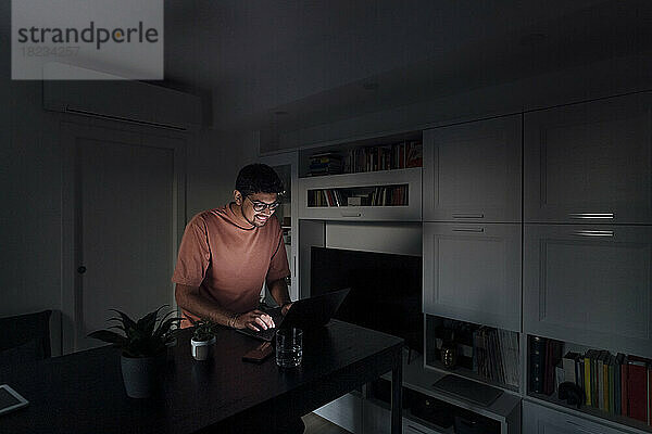 Lächelnder Mann benutzt Laptop im Wohnzimmer zu Hause