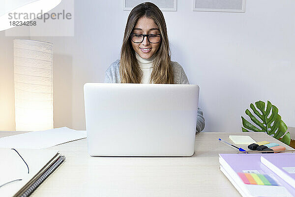 Glückliche junge Frau  die am Schreibtisch am Laptop lernt
