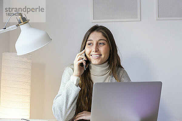 Lächelnde junge Frau  die zu Hause mit dem Smartphone spricht