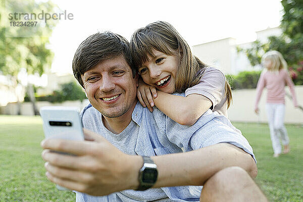 Glückliche Tochter und Vater nutzen Smartphone im Park