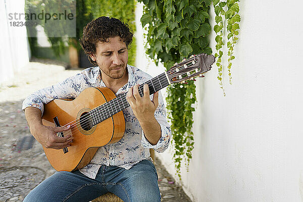 Flamenco-Gitarrist tritt vor einer weißen Wand mit Efeupflanzen auf
