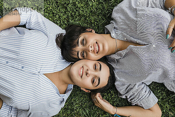 Lesbian couple lying with cheek to cheek on grass