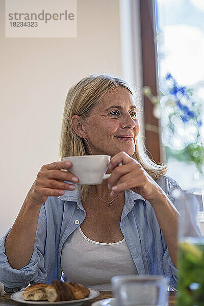 Lächelnde reife Frau hält zu Hause eine Tasse Kaffee