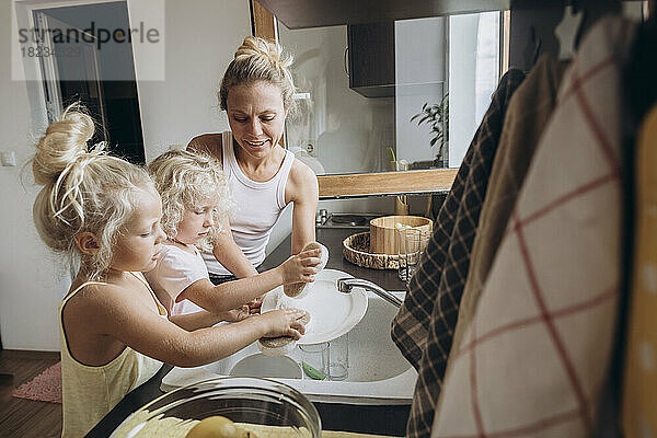 Woman with daughters washing dishes in the kitchen