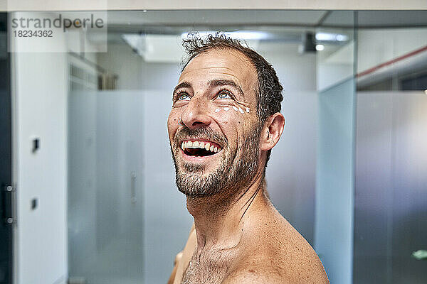 Fröhlicher Mann mit Feuchtigkeitscreme im Gesicht im Badezimmer zu Hause