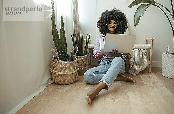 Junge Frau sitzt mit Laptop auf dem Boden im Wohnzimmer