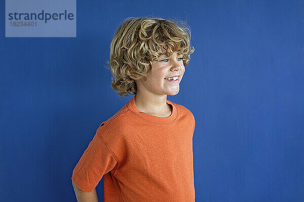 Lächelnder Junge mit orangefarbenem T-Shirt vor blauem Hintergrund