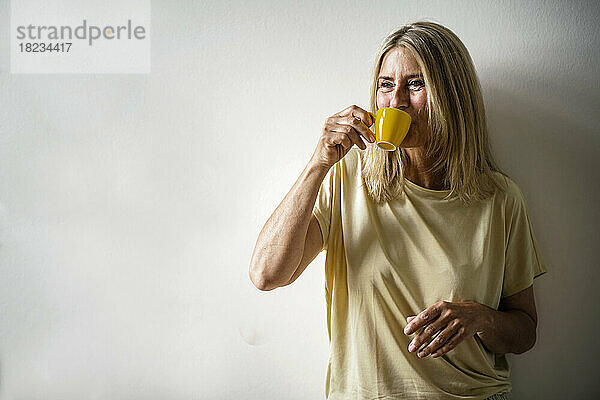 Reife Frau trinkt Kaffee vor der Wand